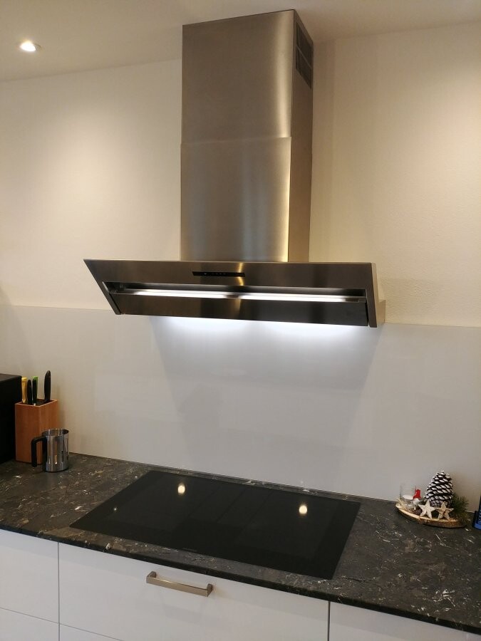 Moderne Küche mit Edelstahl-Dunstabzug über Induktionskochfeld und dunkler Steinplatte.