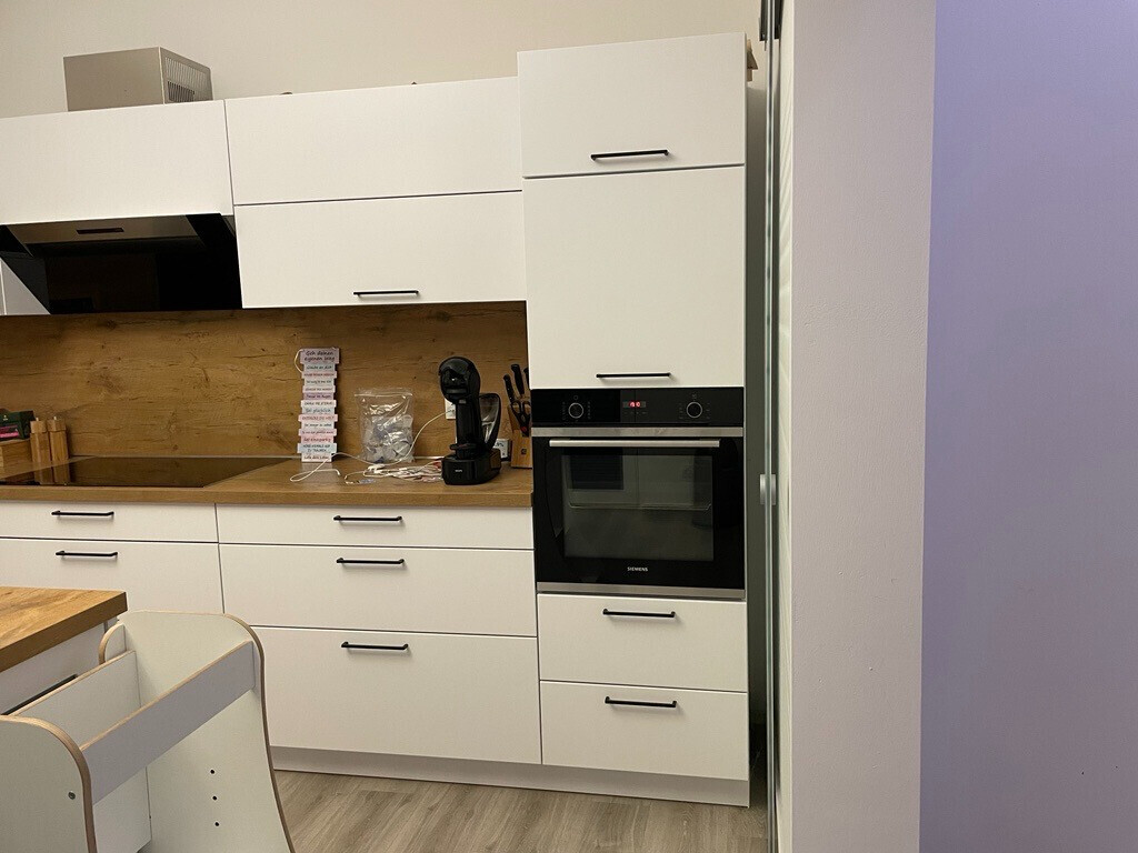 Moderne weiße Küchenzeile mit Backofen, Kaffeemaschine und Holz-Arbeitsplatte.