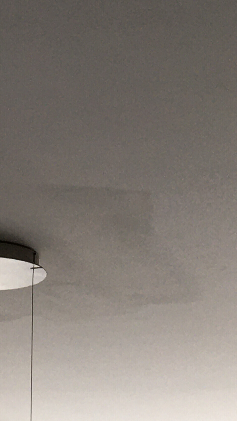 Hängende runde Deckenlampe mit dünnem Kabel vor grauem Hintergrund