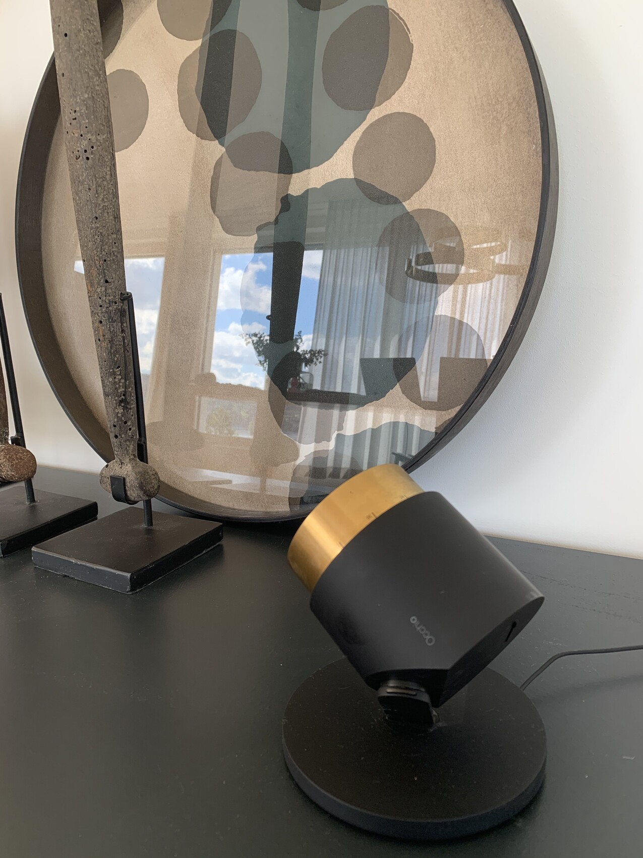 Runder Spiegel mit abstrakter Musterung und einer schwarzen Lampe mit goldener Kappe.