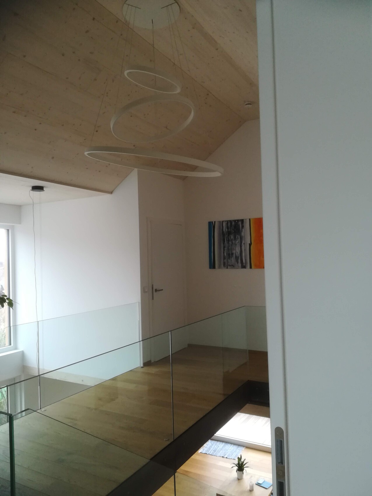 Moderne Loft-Szene: Holzdecke, Glasgeländer, kreisrunde Leuchten, Wandbild.