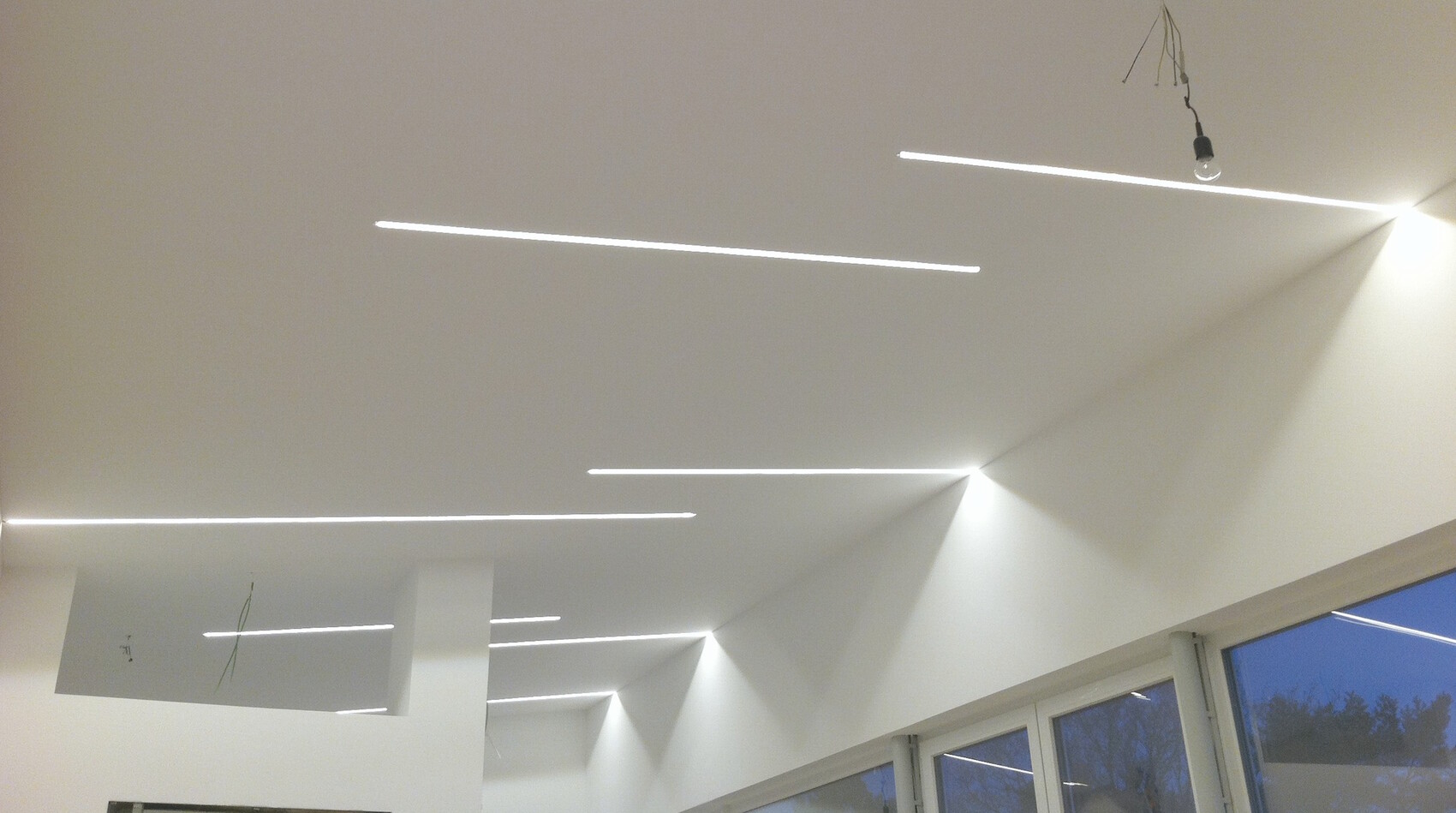 Moderne LED-Deckenbeleuchtung mit schmalen Linien im Innenraum und Fenstern.