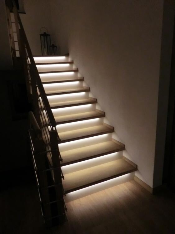 Moderne Holztreppe mit LED-Unterstufenbeleuchtung im dunklen Innenraum.