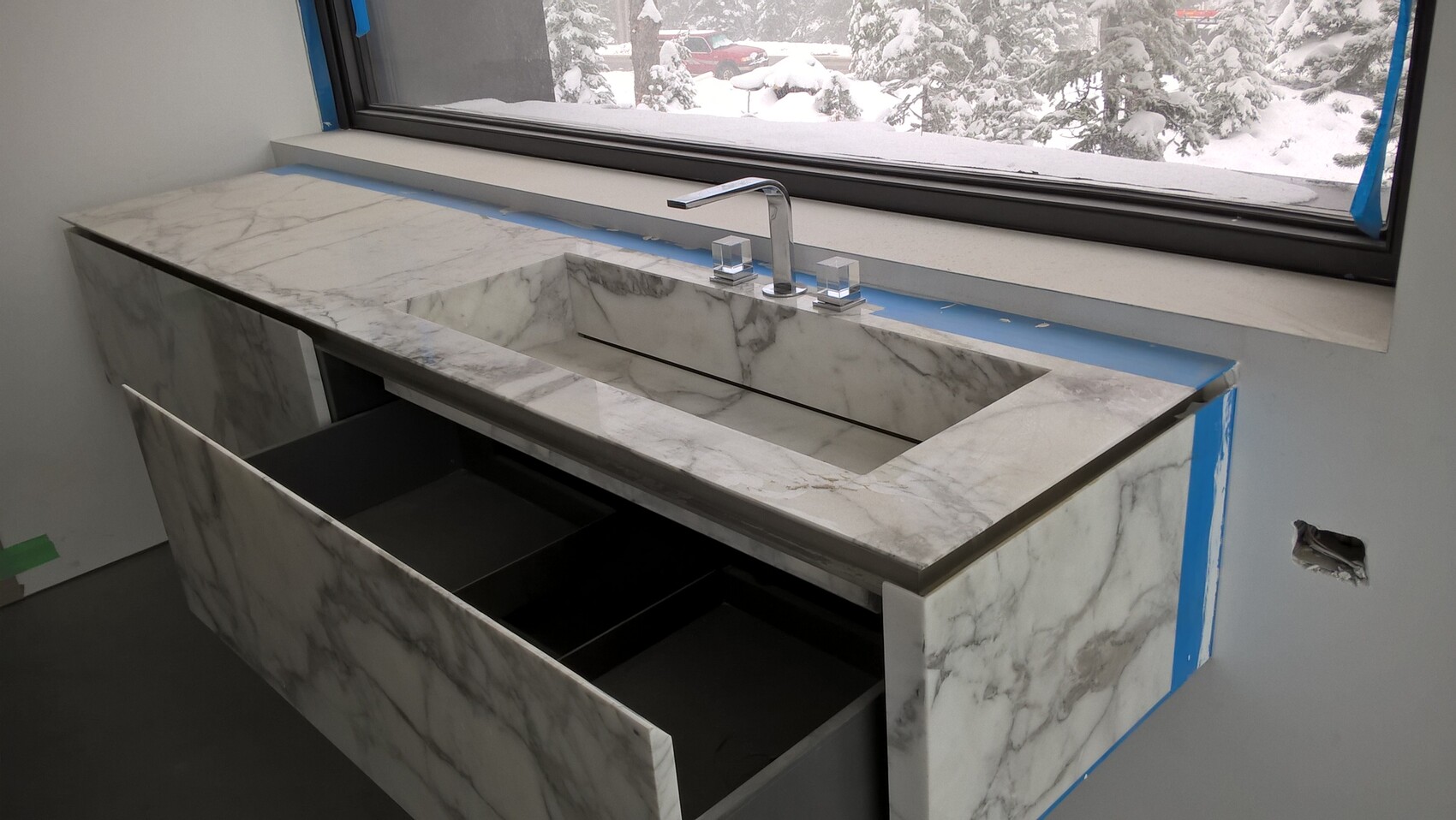 Moderne Marmor-Arbeitsplatte mit eingebettetem Waschbecken, offene Schublade, verschneites Fenster.