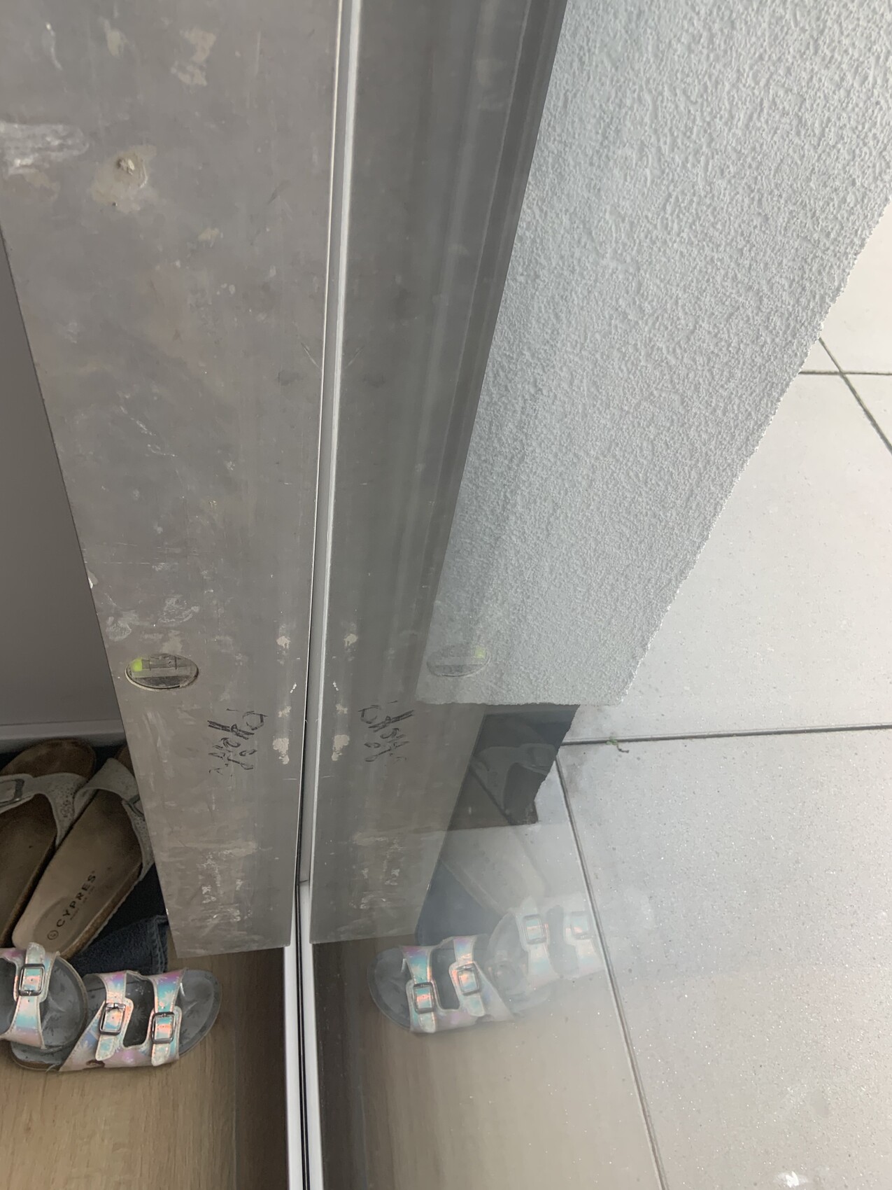 Aufzugstür aus Metall mit Kratzern; Sandalen unten links, Außenfliesen rechts.