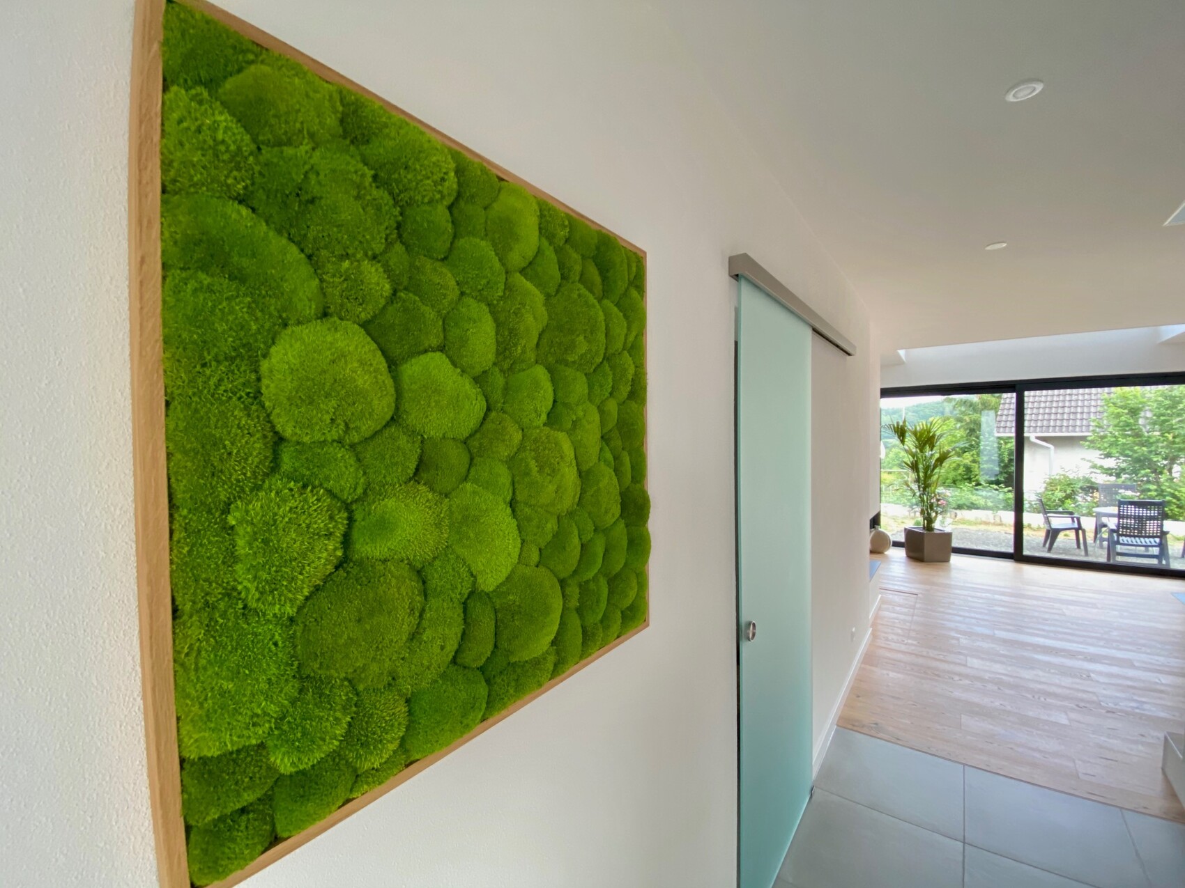 Grünes Moos-Wandbild in Holzrahmen an Flurwand neben einer gläsernen Schiebetür.