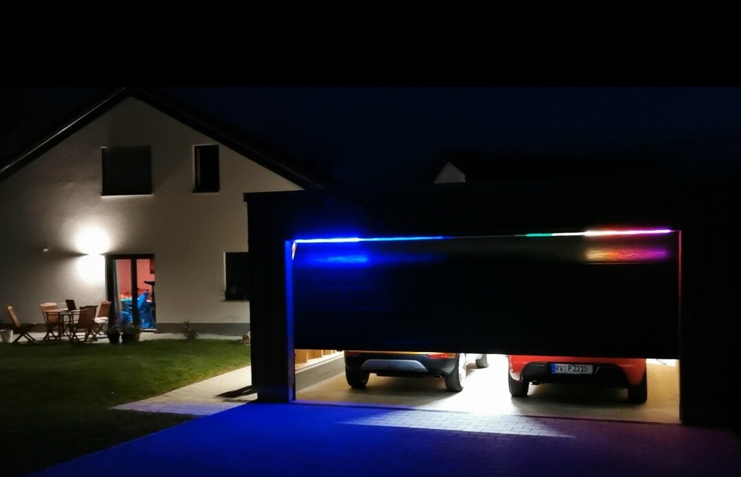 Nachtaufnahme: Garage mit zwei Autos und bunten LED-Leisten, beleuchtete Einfahrt.