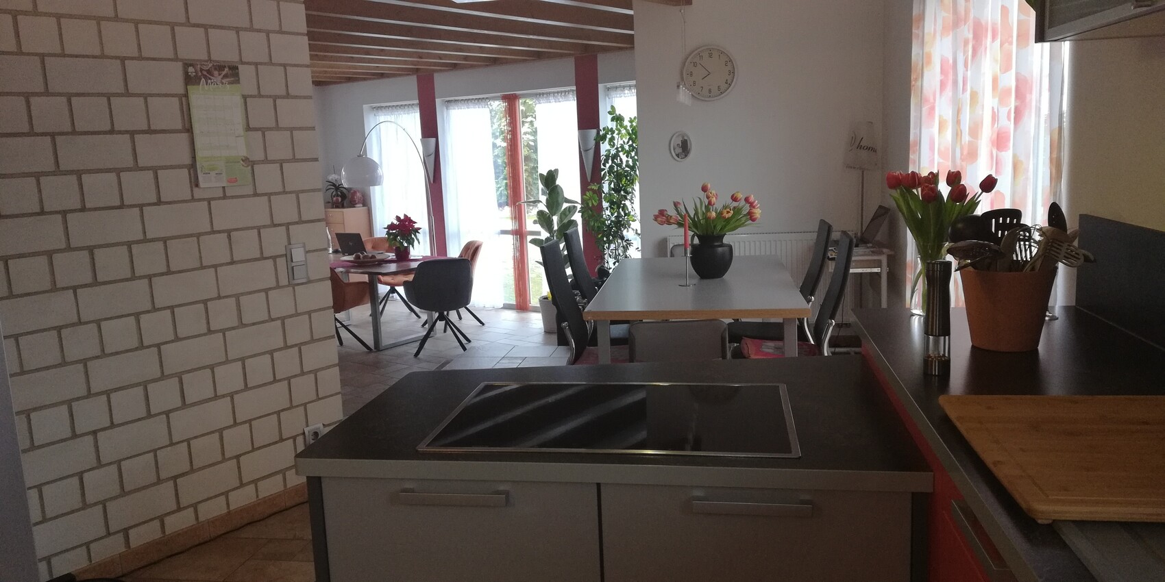 Offene Küche mit Kochinsel, Esstisch, Tulpen und Zimmerpflanzen am Fenster.