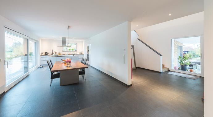 Großer offener Wohn- und Essbereich mit Esstisch, Küche im Hintergrund, Treppe und Terrasse.