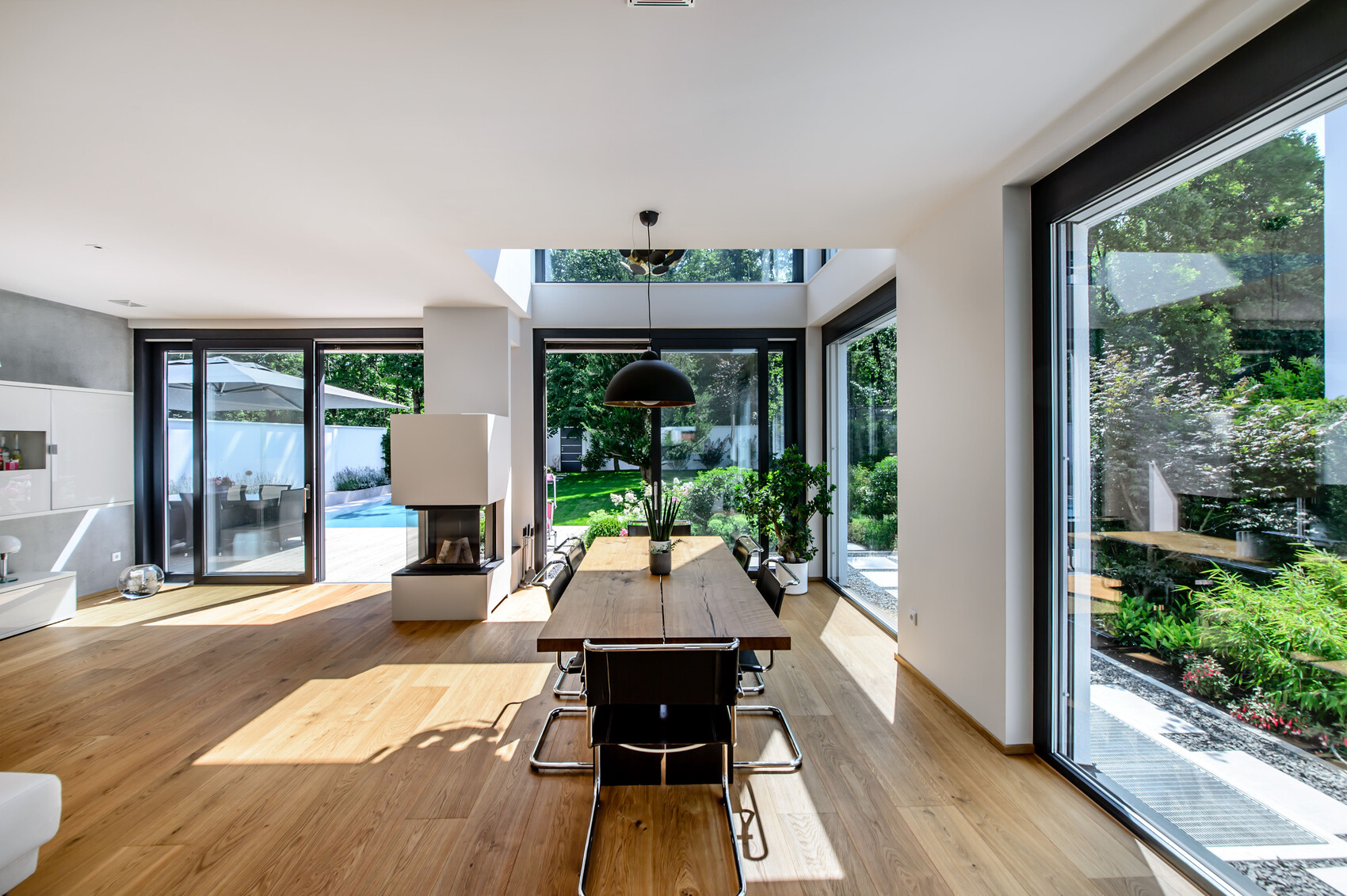 Moderne Esszimmer: langer Holztisch, schwarze Stühle, Kamin, große Fenster mit Gartenblick.