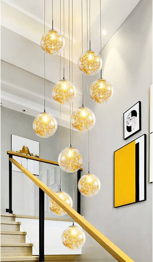 Mehrere gelbe Glaskugelleuchten hängen über einer Holztreppe mit Geländer und Wandkunst.