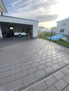 Gepflasterter Vorplatz vor Garage mit Parkfläche, Drainagerinne und angrenzendem Garten.
