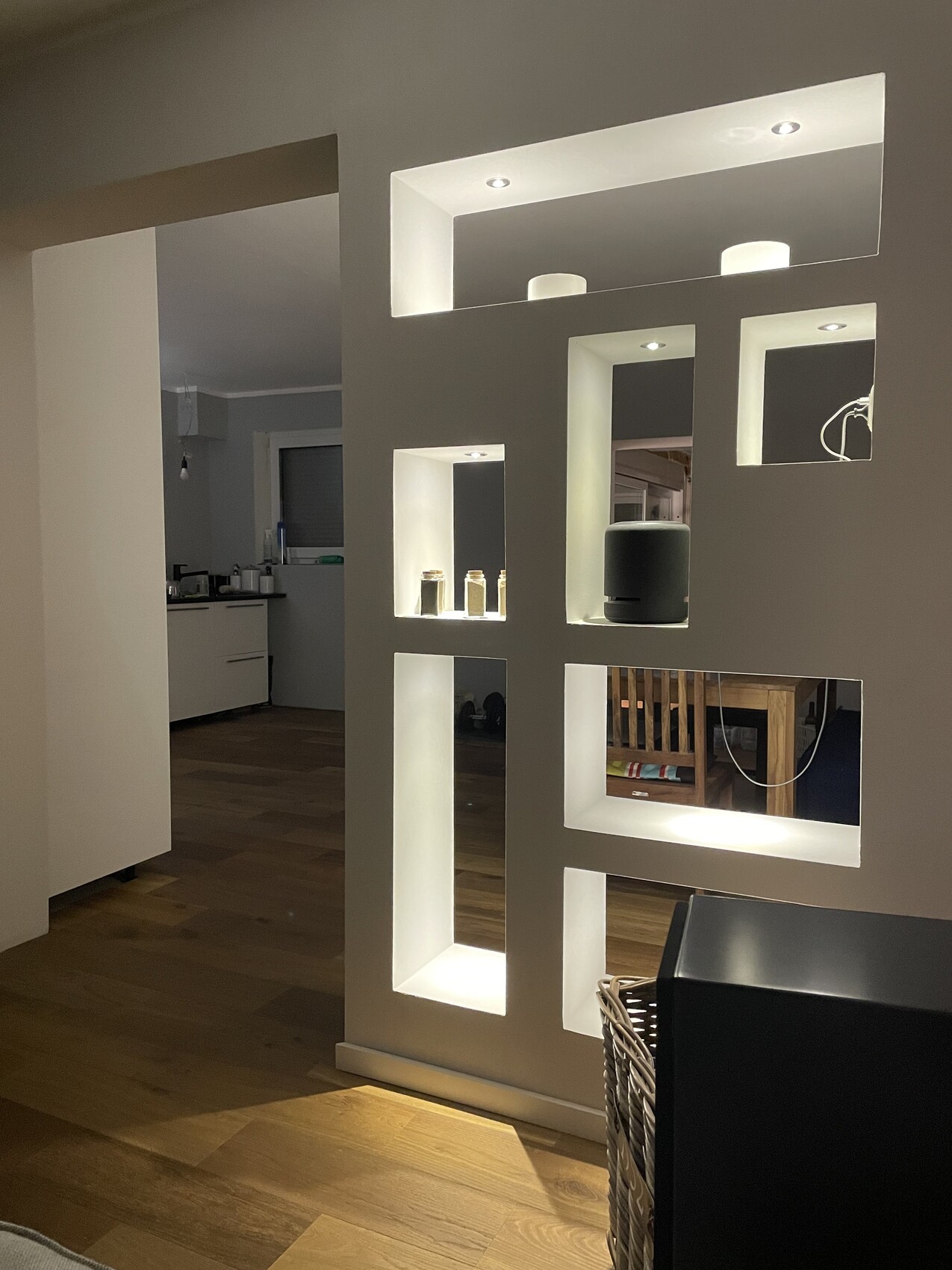 Moderne Trennwand mit beleuchteten Nischen, Blick auf offene Küche und Holzfußboden.