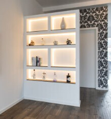 Moderne Regalwand mit LED-Beleuchtung und dekorativen Objekten in hellem Raum.
