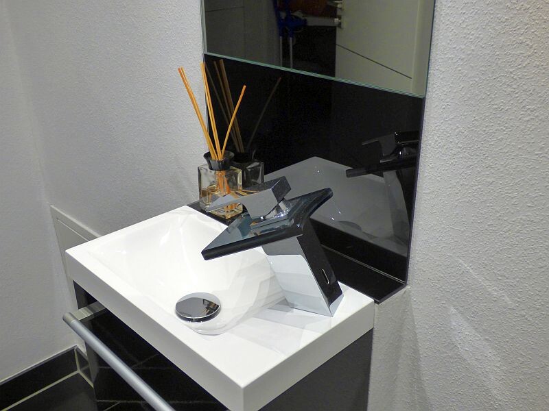 Moderner Waschplatz mit weißem Becken, stilvollem schwarzen Wasserhahn, Spiegel und Duftdiffusor.