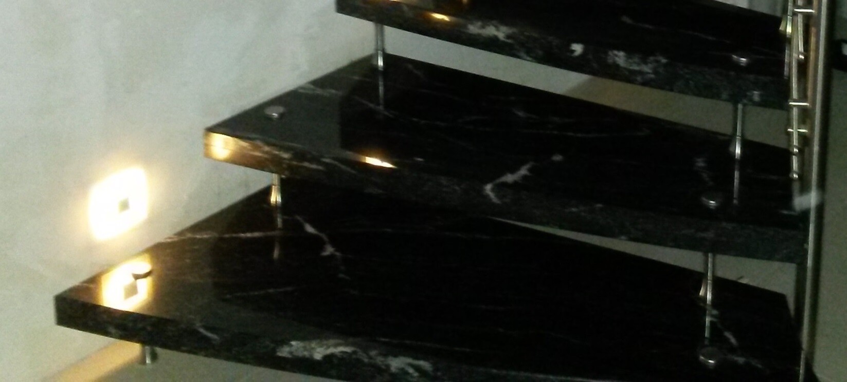 Schwarze Marmortreppen mit Edelstahlstützen und warmen Lichtreflexen an der Wand.