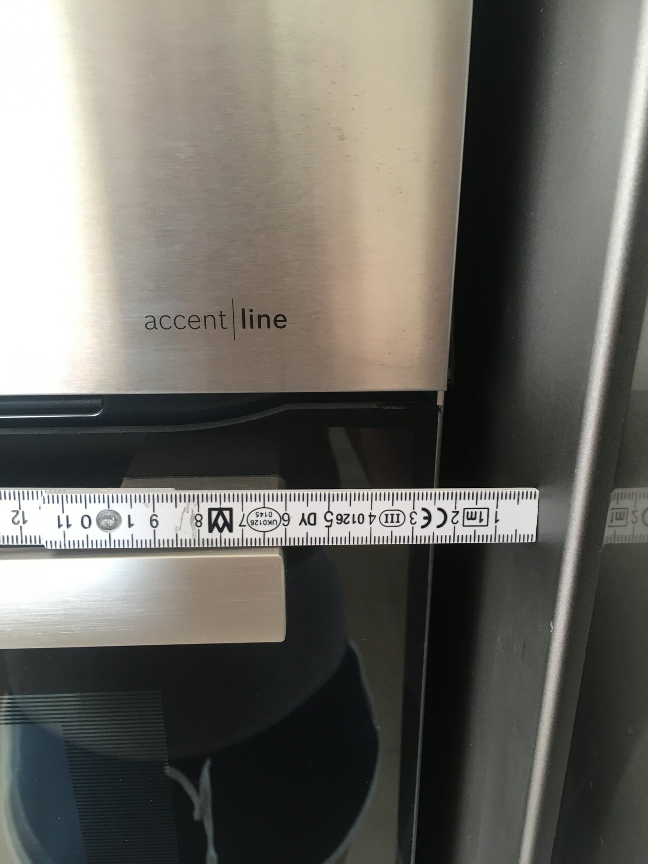 Nahaufnahme eines Edelstahl-Kühlschranks mit Messband und Accent-Line-Logo