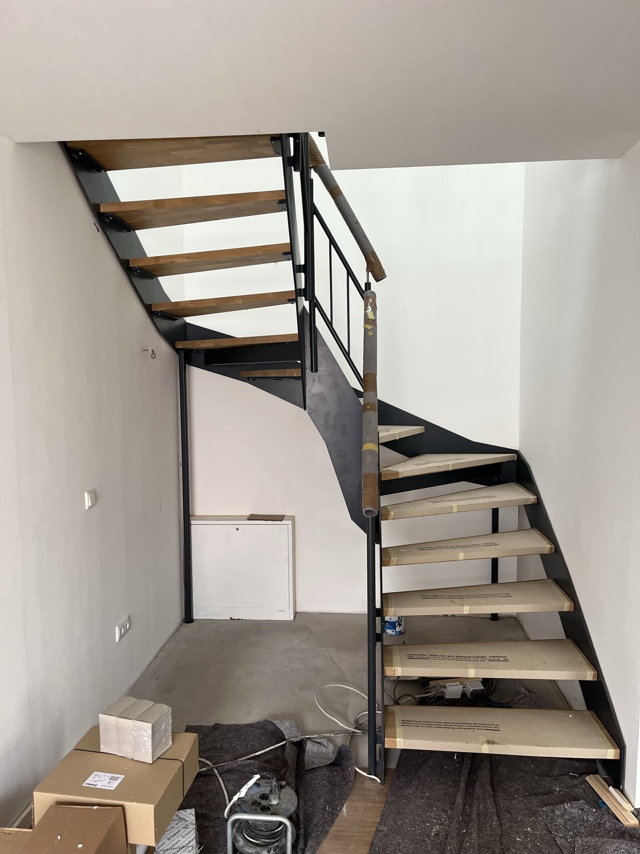 Moderne Metalltreppe mit Holzstufen in Bauzustand; Kartons und Werkzeuge im Raum.