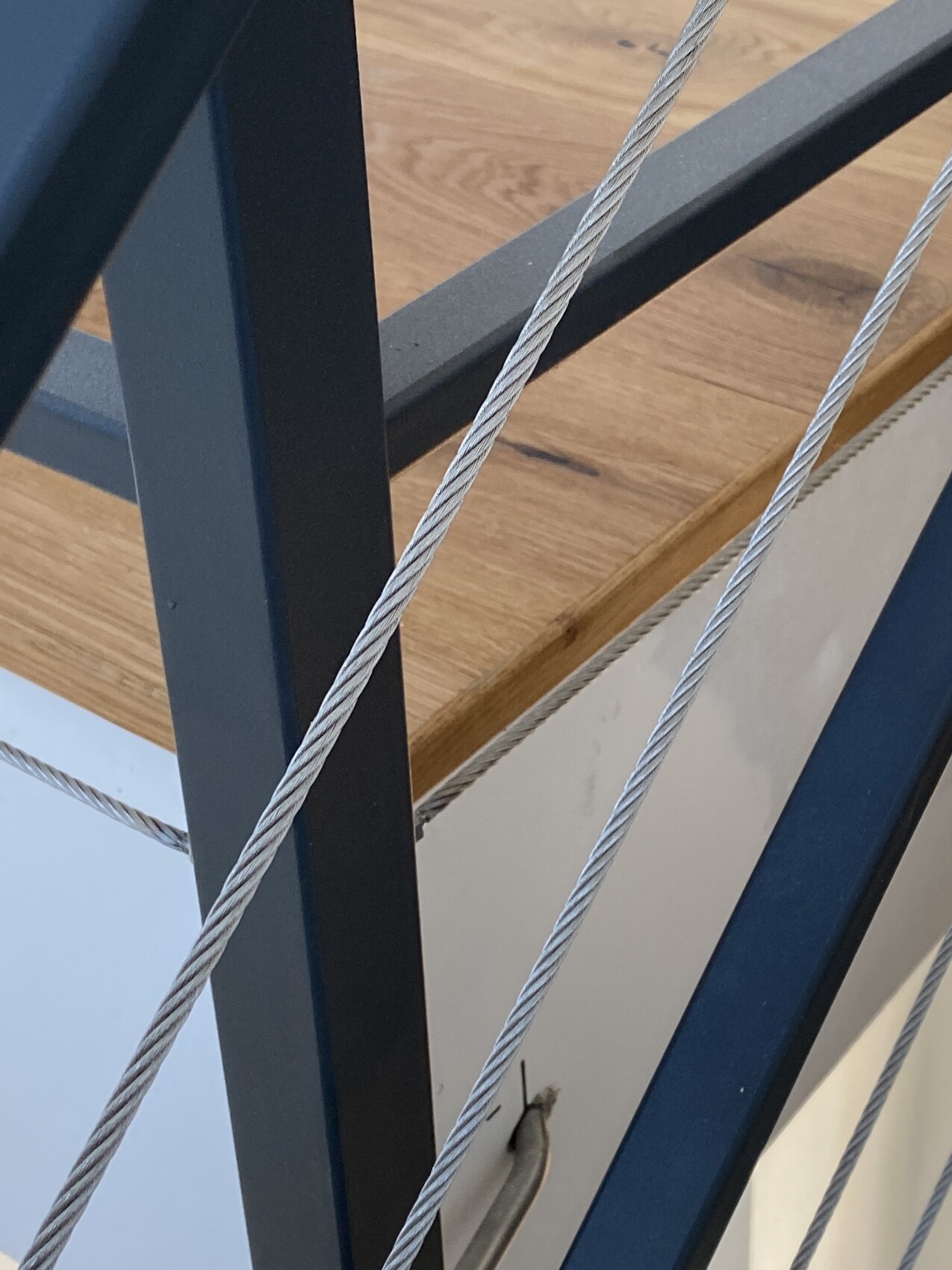 Nahaufnahme einer Treppe: blaue Stahlrahmen, Drahtseile und Holzstufen.
