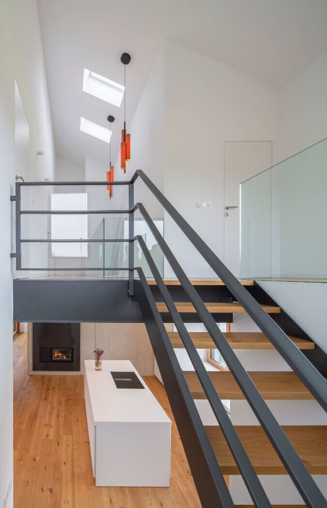 Moderne Loft-Szene: Treppe mit schwarzen Geländern, Glasbrüstung, Holzstufen, orange Pendelleuchten.