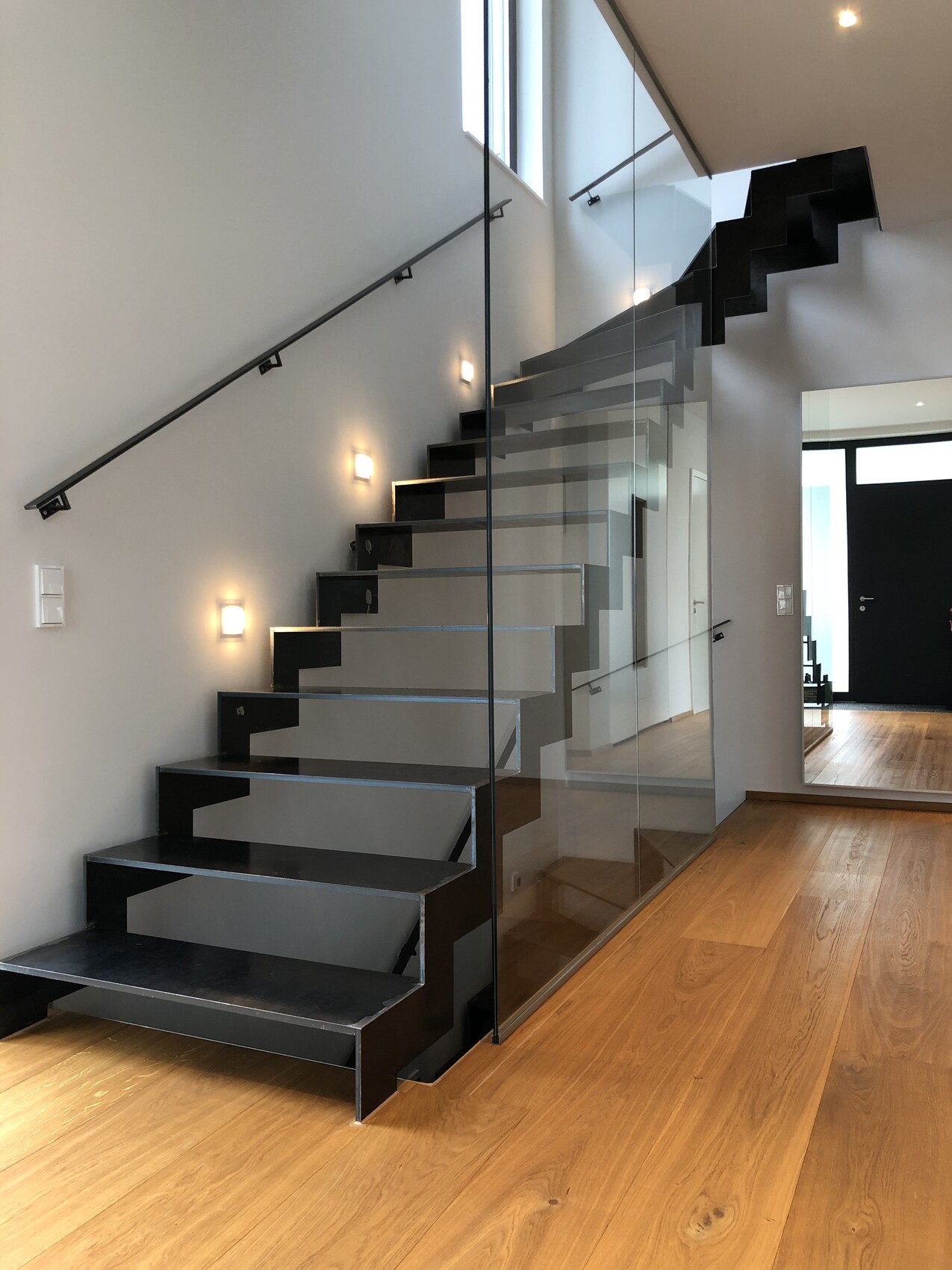 Moderne Innentreppe mit schwarzen Stufen, glasgaender und holzboden im flur.
