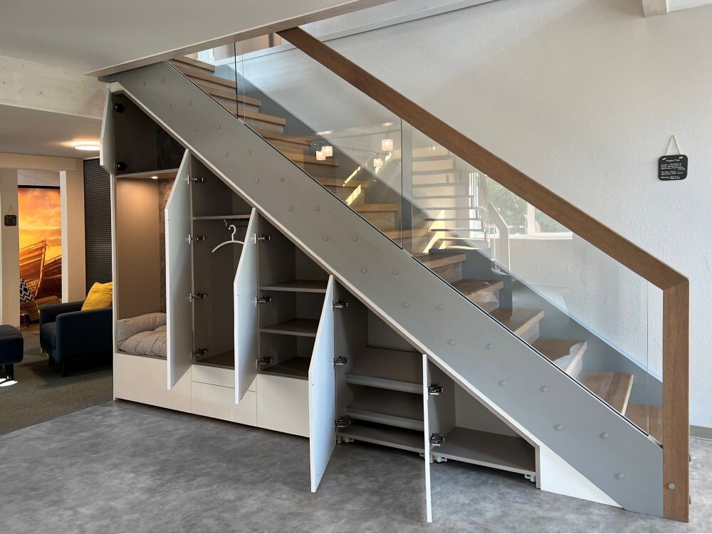 Moderne Innenansicht: Treppe mit Glasgeländer, darunter offene Schränke und Regale unter der Treppe.