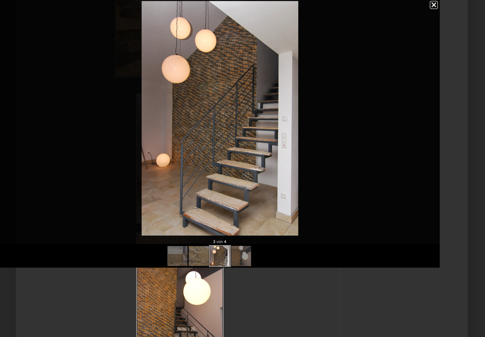 Moderne Treppe mit offenen Holzstufen und Metallrahmen; vor gemusterter Wand hängen Pendellampen.