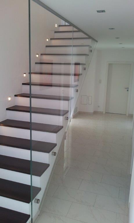Moderne Innentreppe mit dunklen Holzstufen und Glasgeländer in hellem Flur.
