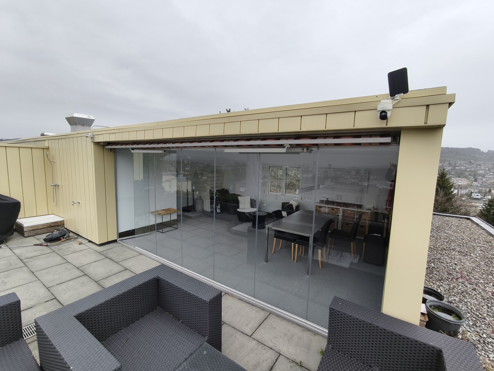 Dachterasse mit großen Glas-Schiebetüren, gelbe Fassade, dunkle Rattan-Sitzgruppe, Stadtblick