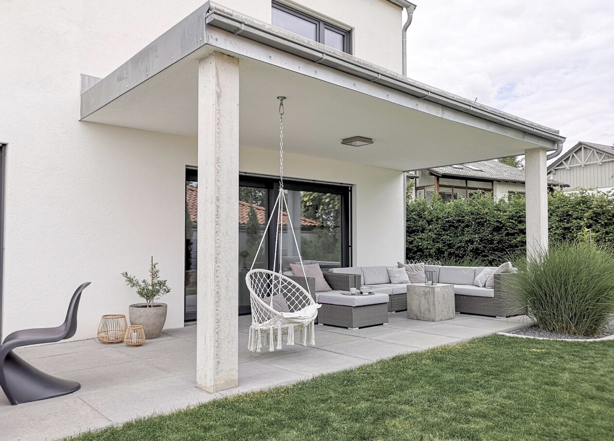 Überdachte Terrasse mit Hängesessel, grauer Lounge-Ecke, Pflanze und Laternen