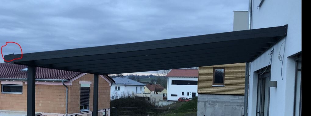 Eine schwarze Metall-Pergola über einer Terrasse; im linken Rand eine kleine graue Box.