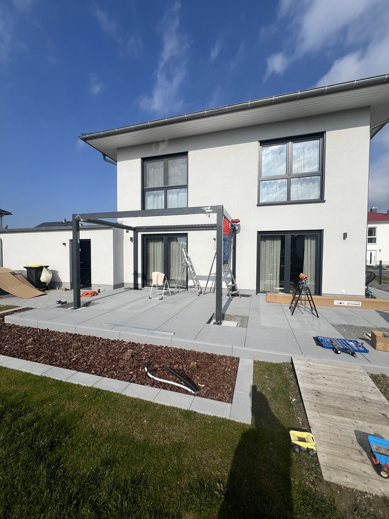 Modernes weißes Haus mit Glas-Schiebetüren; Bau einer Pergola auf Terrasse, Arbeiter auf Leiter