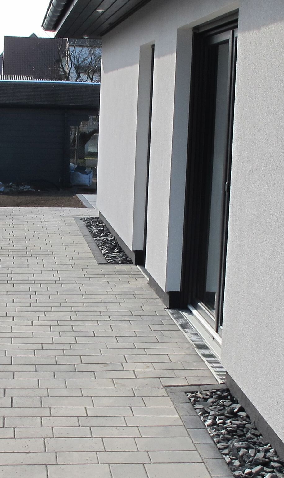 Moderne weiße Fassadenfront mit großen Glas-Schiebetüren, gepflastertem Vorplatz und Kiesstreifen.