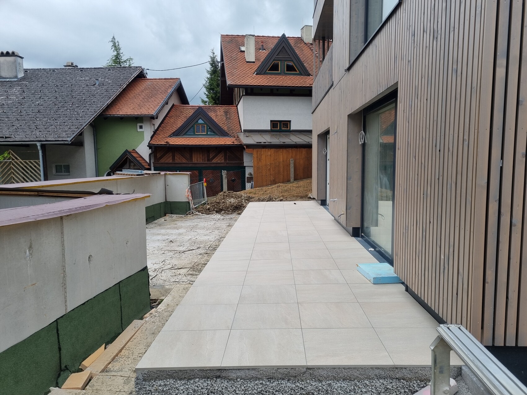 Neubau mit moderner Terrasse aus Platten neben einem Holzhaus, Bauarbeiten im Hof