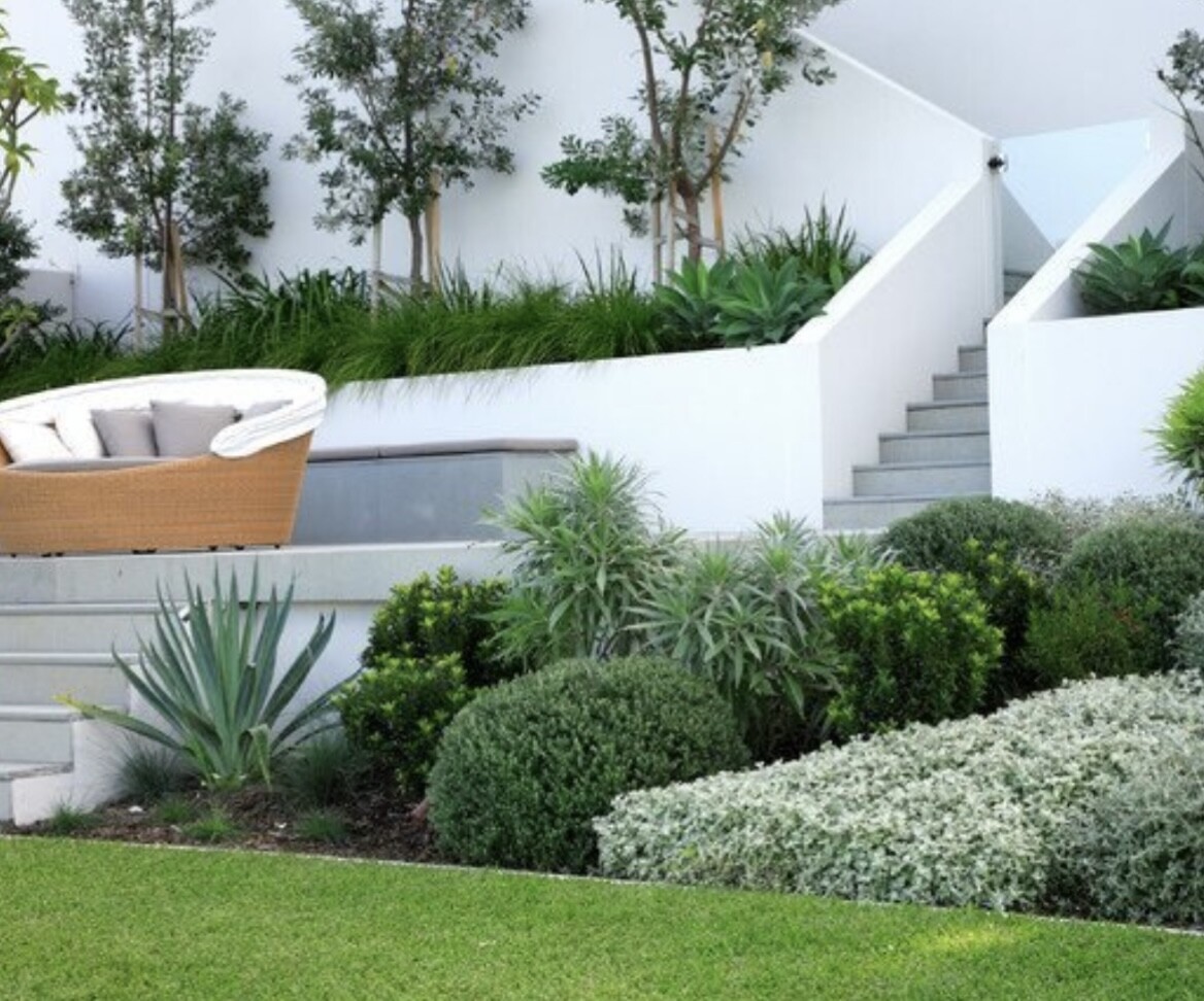 Moderne Terrasse mit weißen Mauern, Stufen, Lounge-Sessel und grünem Garten.