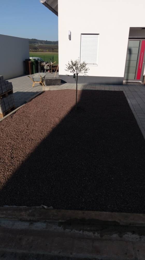 Moderne Hausfront mit Hof aus Kies, kleinem Baum, Sitzgruppe und roter Tür.