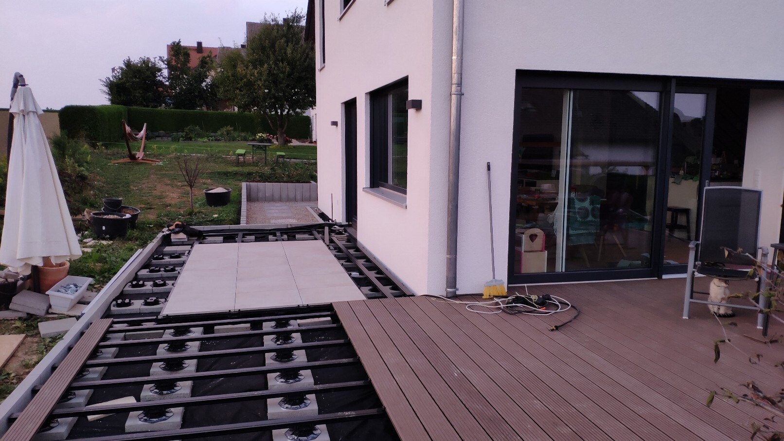 Teilweise fertige Terrassenkonstruktion am Haus, Garten mit Hängematte und Sonnenschirm