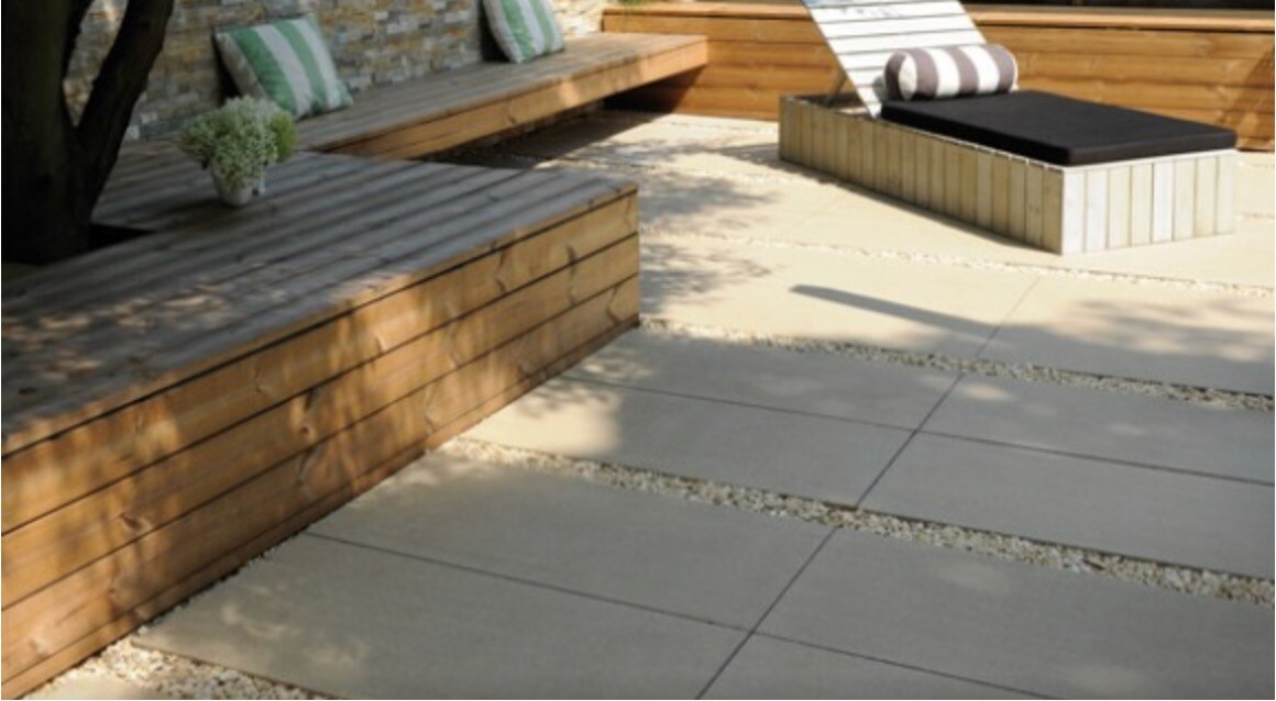 Garten-Terrasse mit Holzbank, Pflanze, Lounge-Sessel und sandfarbene Pflasterplatten.