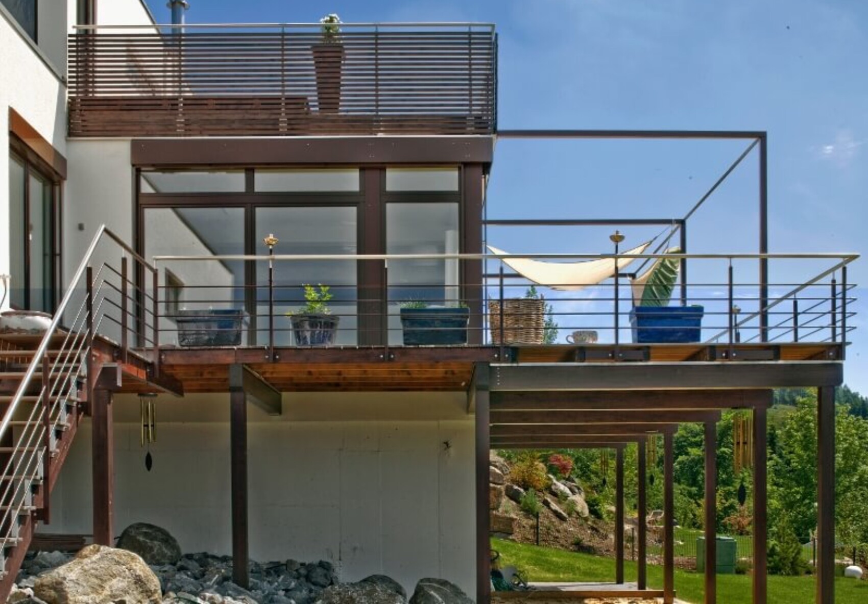 Moderne mehrstöckige Terrasse eines Hauses mit Metallgeländer, Pflanzkübeln und Hängematte