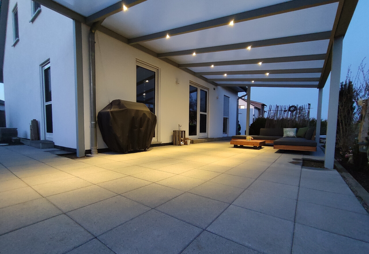 Moderne Terrasse mit Pergola, beleuchteten Bodenplatten, abgedecktem Grill und Lounge-Möbel.