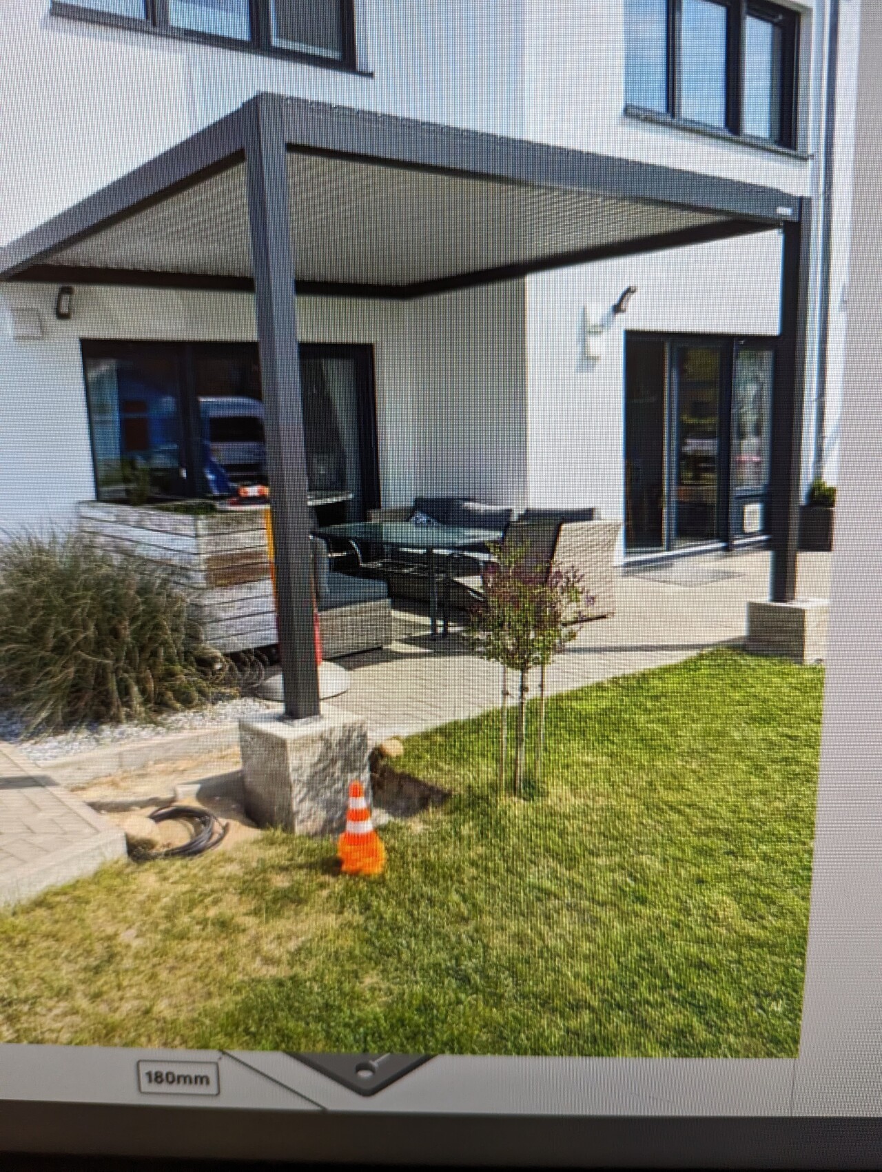 Moderne weiße Hausfassade mit überdachter Terrasse, Glas-Tisch und Gartenmöbeln.