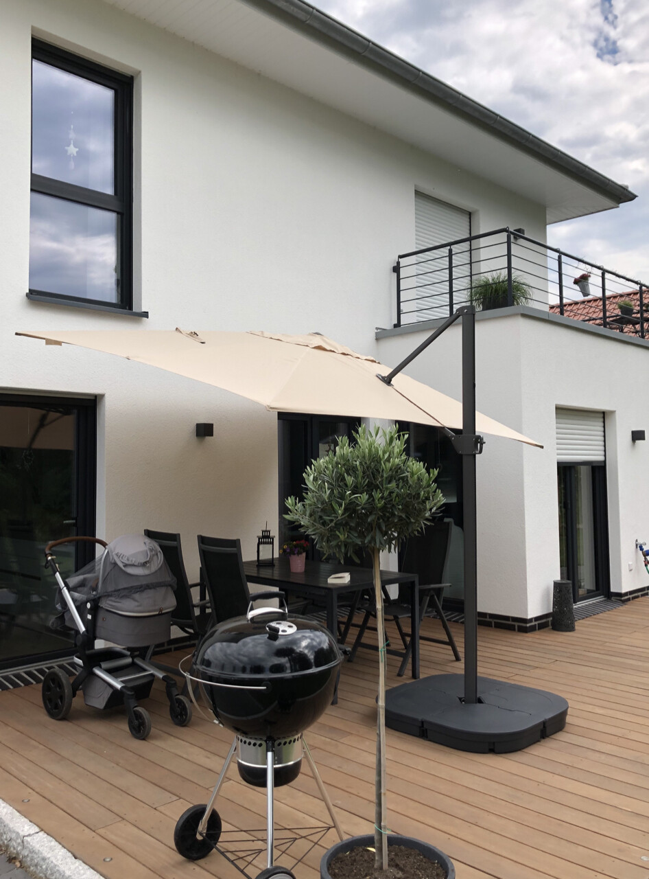Moderne Patio-Szene: Esstisch mit Stühlen, großer Sonnenschirm, Grill und Kinderwagen auf Holzdiele.