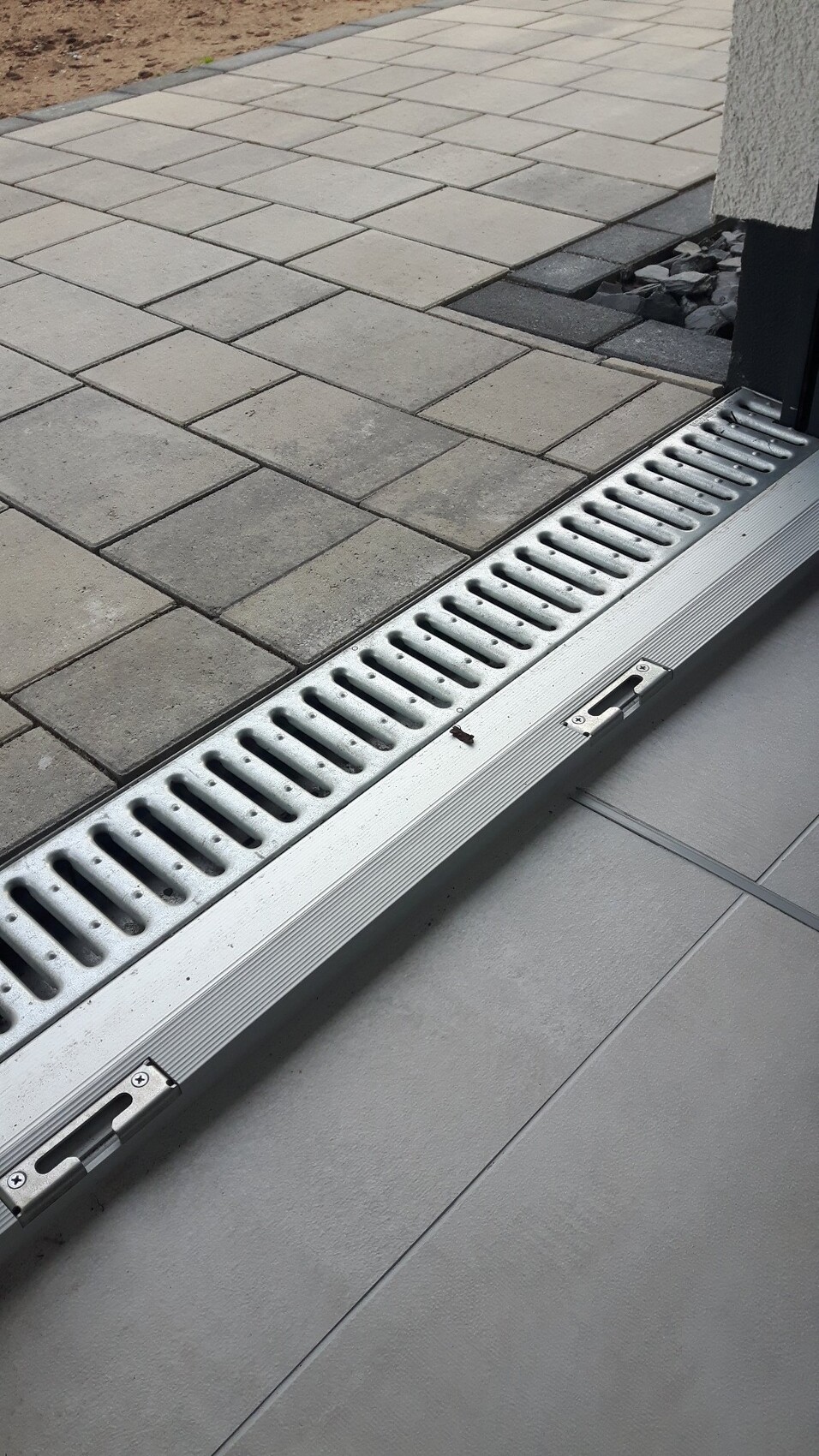 Metallrinnenablauf am Übergang von gepflastertem Außenbereich zu Fliesenboden.
