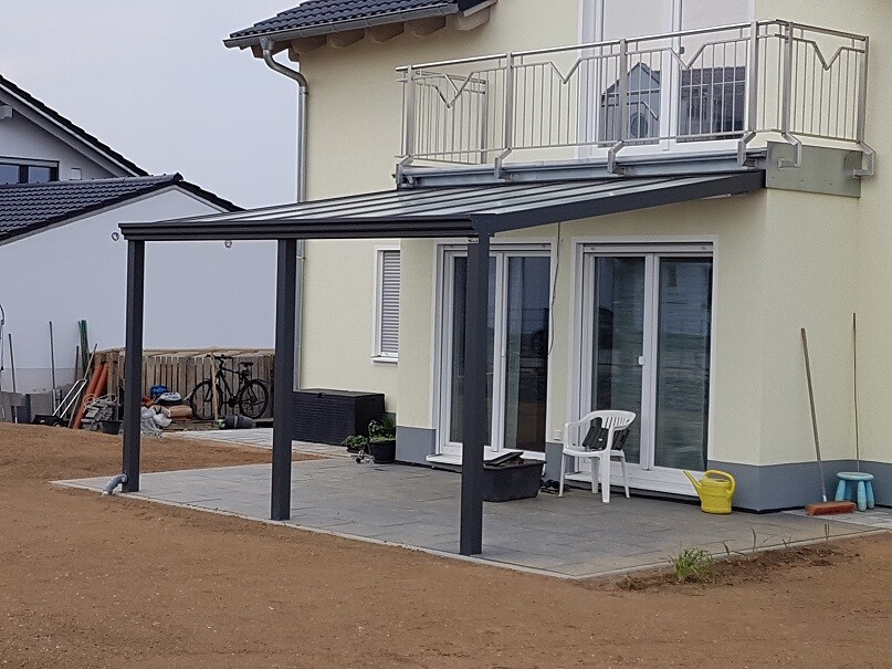 Garten-Terrasse eines Hauses mit Pergola, Balkon oben und Glasschiebetüren.