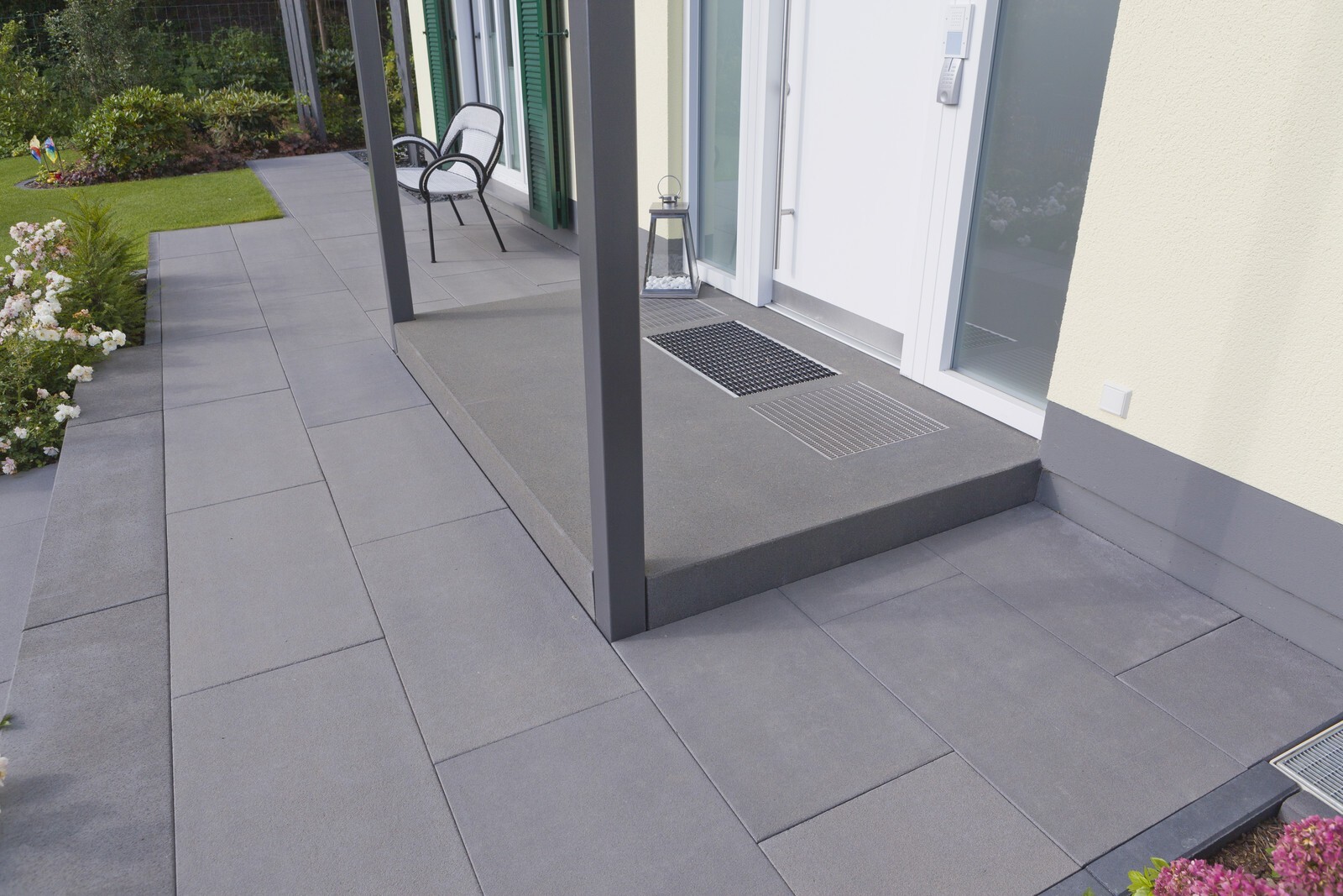 Moderne Terrasse vor einem Haus: graue Großformat-Pflasterplatten, Stuhl, Laterne und Glastür.