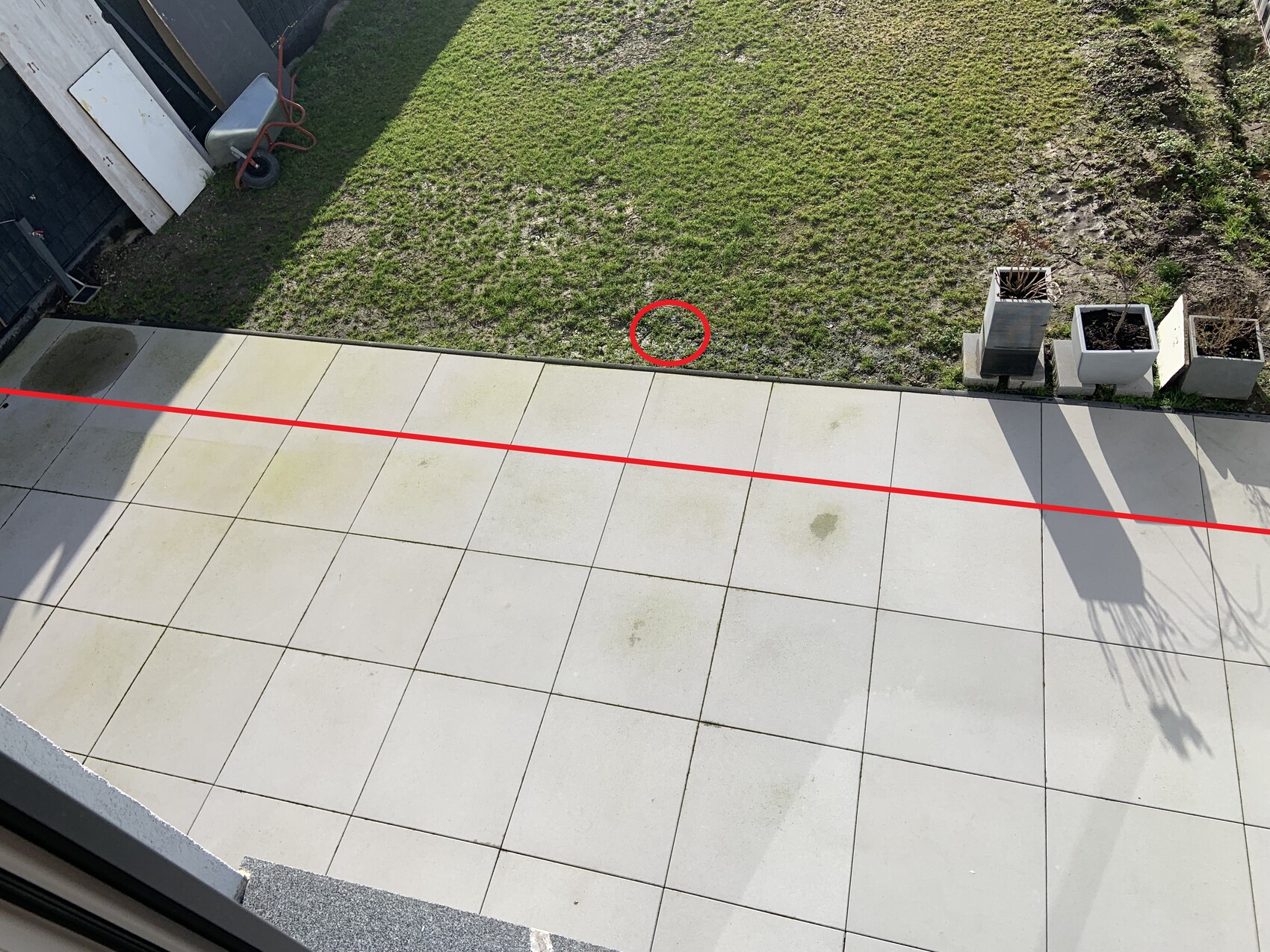 Außenbereich mit heller Terrassenfläche, Rasen und Pflanzkübeln; Markierung sichtbar.