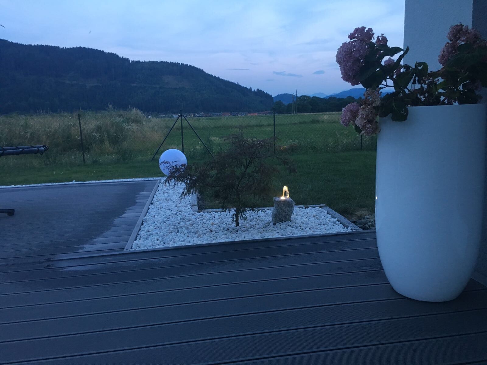 Terrasse mit einer weißen Vase und Hydrangea, Kies, Kerze auf Stein, Blick auf Garten und Berge.
