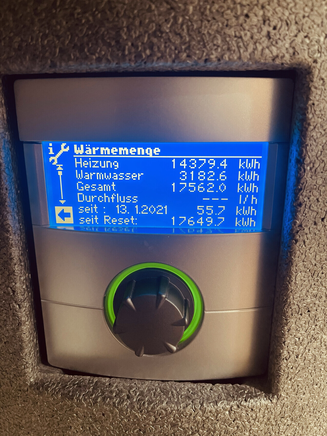 Blaues Display eines Heizungs-/Warmwasserzählers mit Verbrauchswerten in kWh und grünem Knopf.