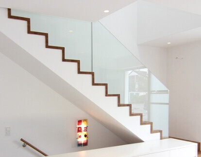 Moderne Treppe mit Glasgeländern in hellem Innenraum, weiße Wände und dunkle Stufen