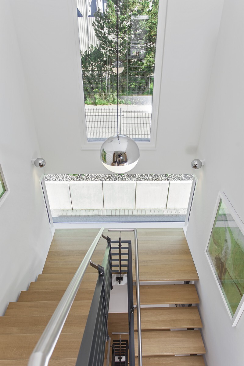 Moderne Holzstufen-Treppe mit Metallgeländer in hellem Innenraum; runde Deckenlampe.